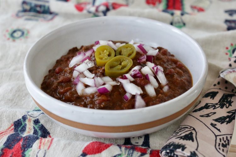 Bowl of vegan chili with onions and pickled jalapeños on top