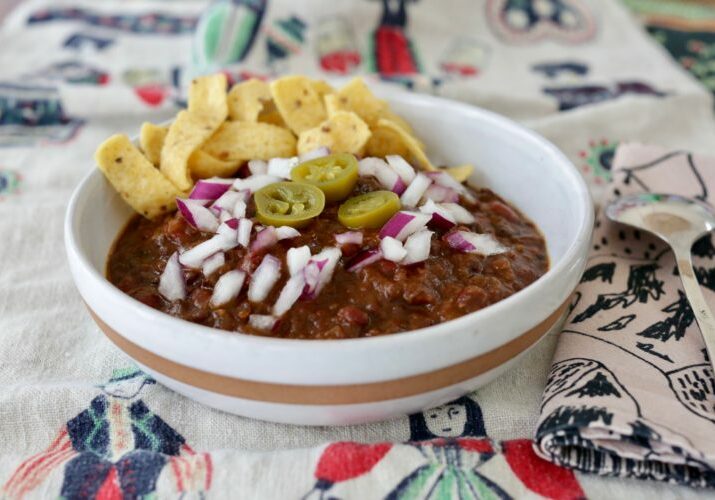 Bowl of vegan chili with onions and pickled jalapeños